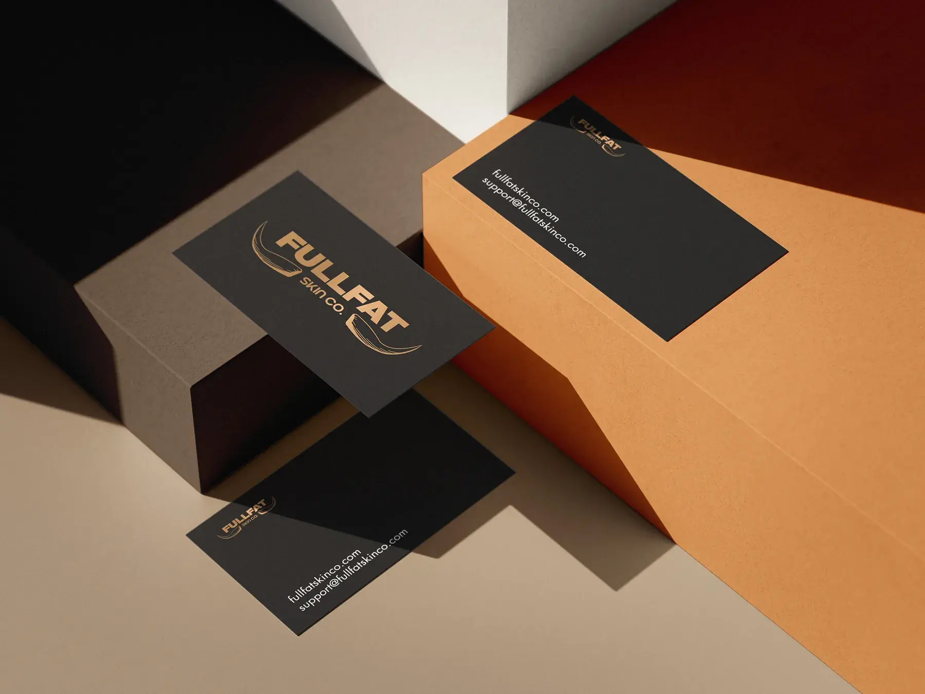 Black business cards with the bronze FULLFAT logo and the fullfatskinco.com address, on warm orange and stone blocks