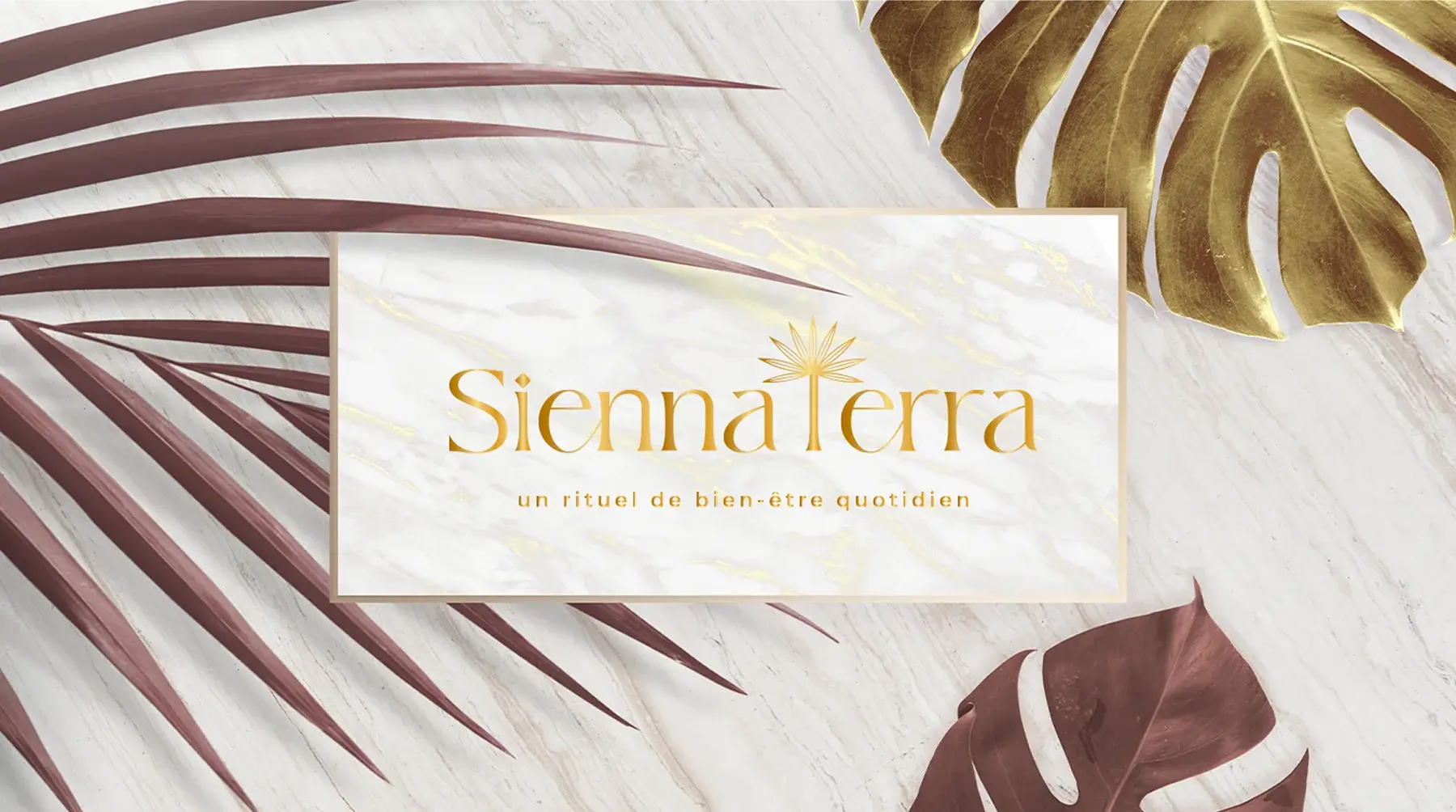The gold-foil Sienna Terra logo on a marble card among monstera and palm leaves