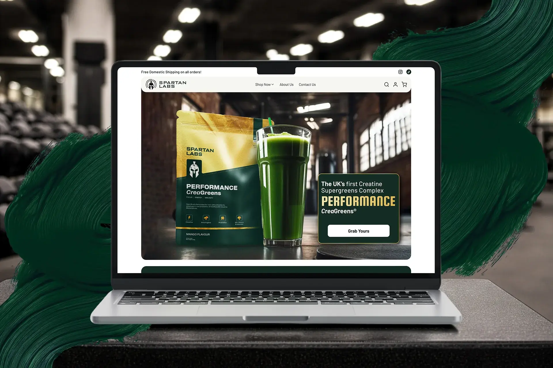Spartan Labs storefront hero on a laptop in a gym setting, the Performance CreaGreens pouch beside a glass of green drink